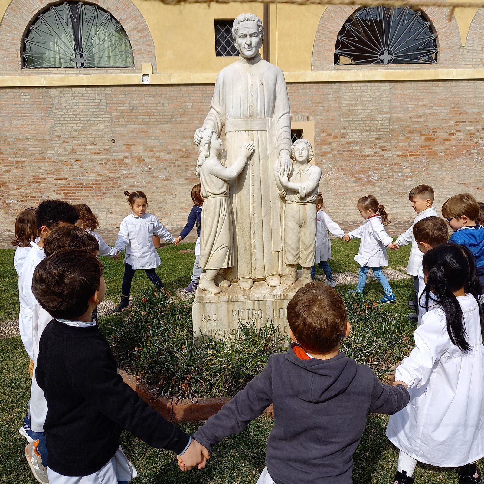 Bambini della scuola nel cortile con la statua di Don Pietro Leonardi